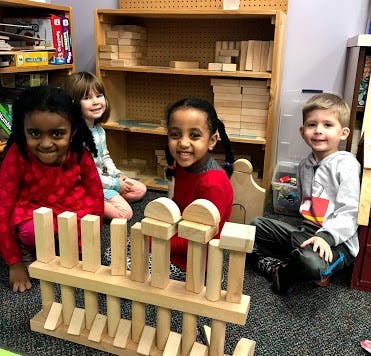 Four children playing with wooden blocks in a classroom