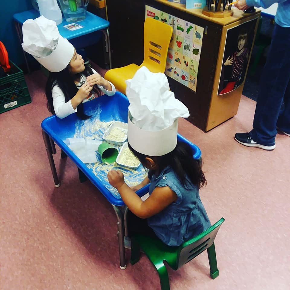 Two children wearing chef hats playing at a table