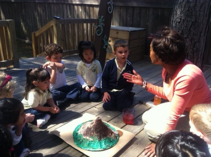 Adult and children sitting on a deck around a volcano model