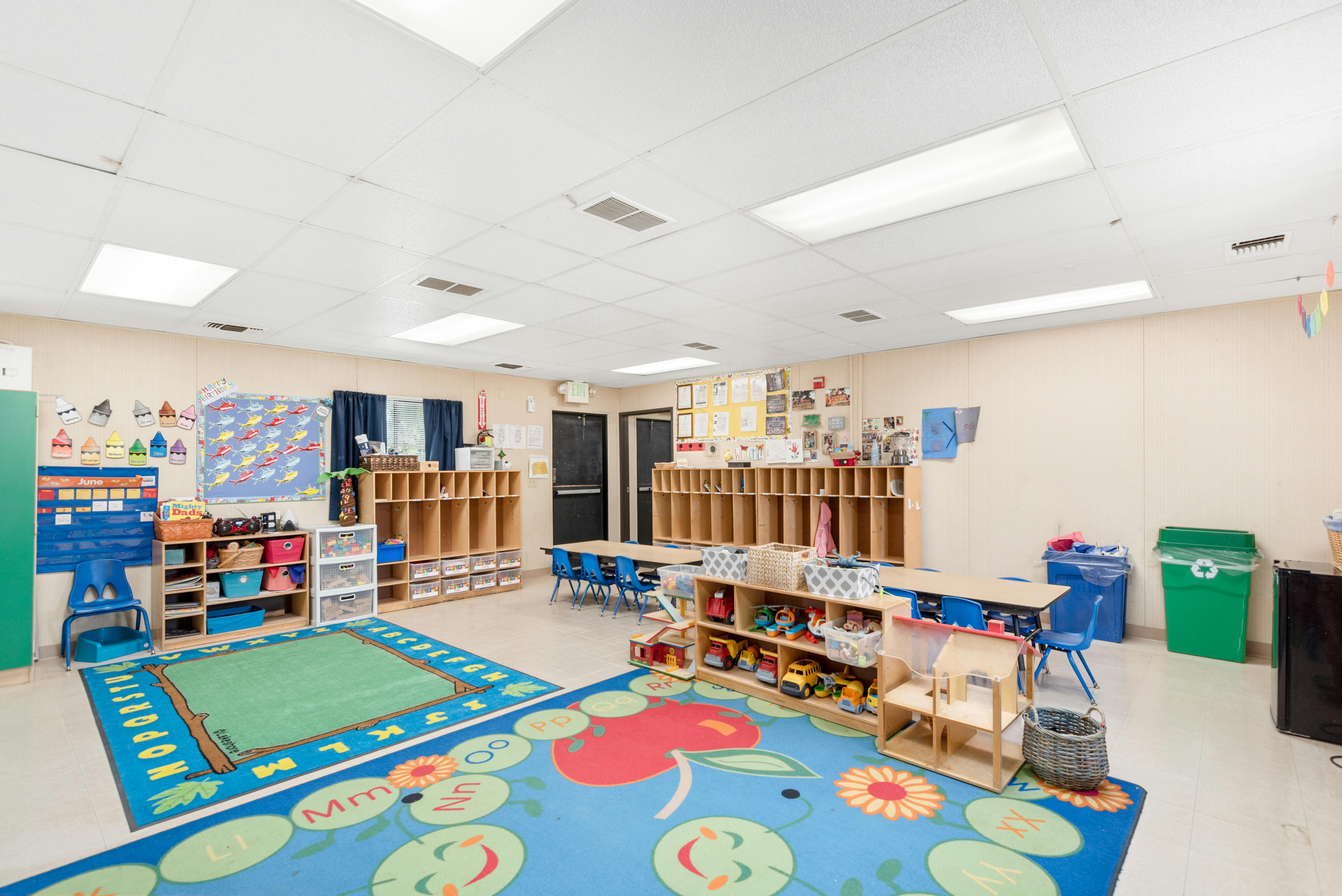 Empty classroom with colorful rugs, small tables, and storage shelves