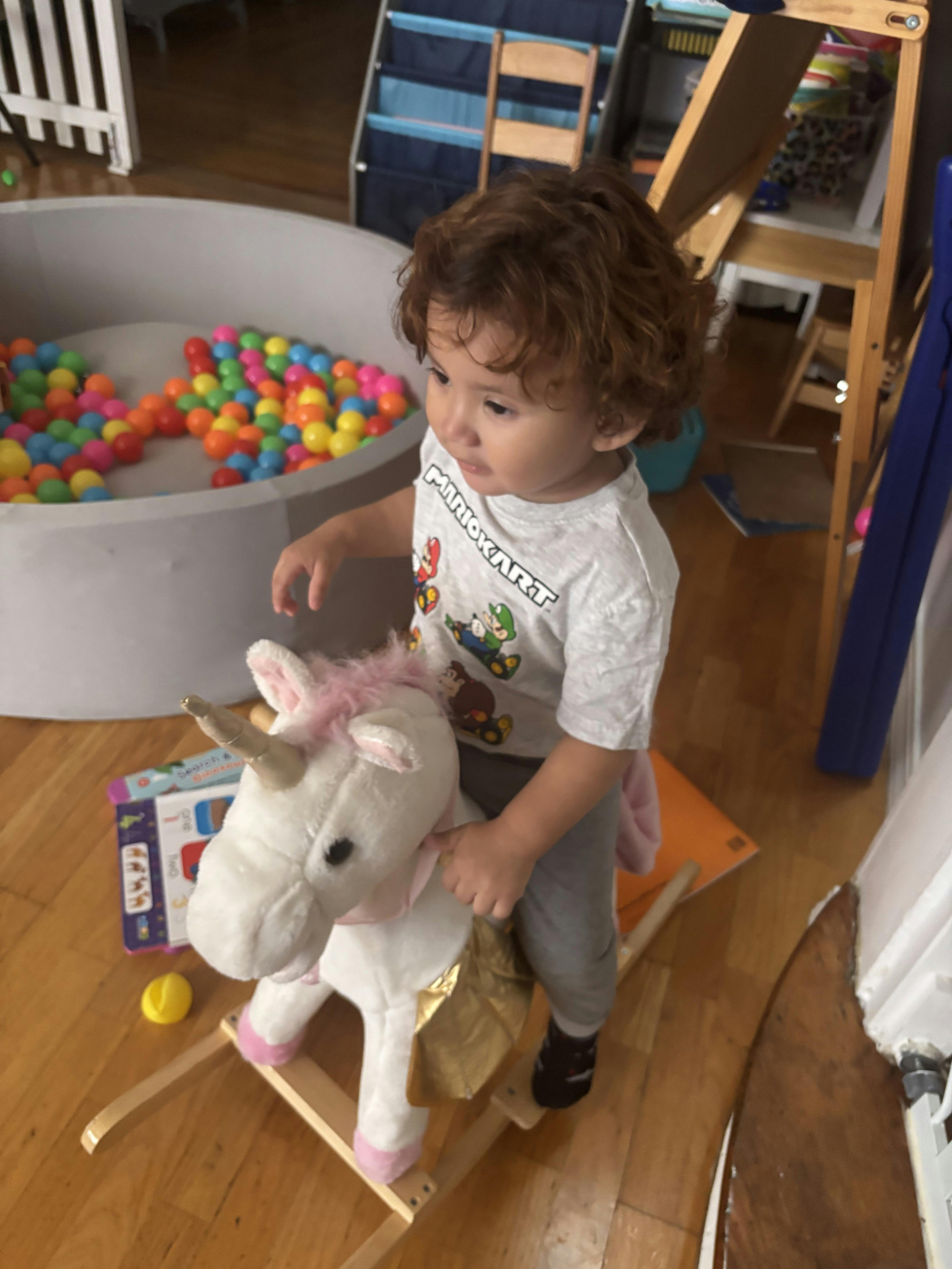 Child sitting on a unicorn rocking toy in a play area