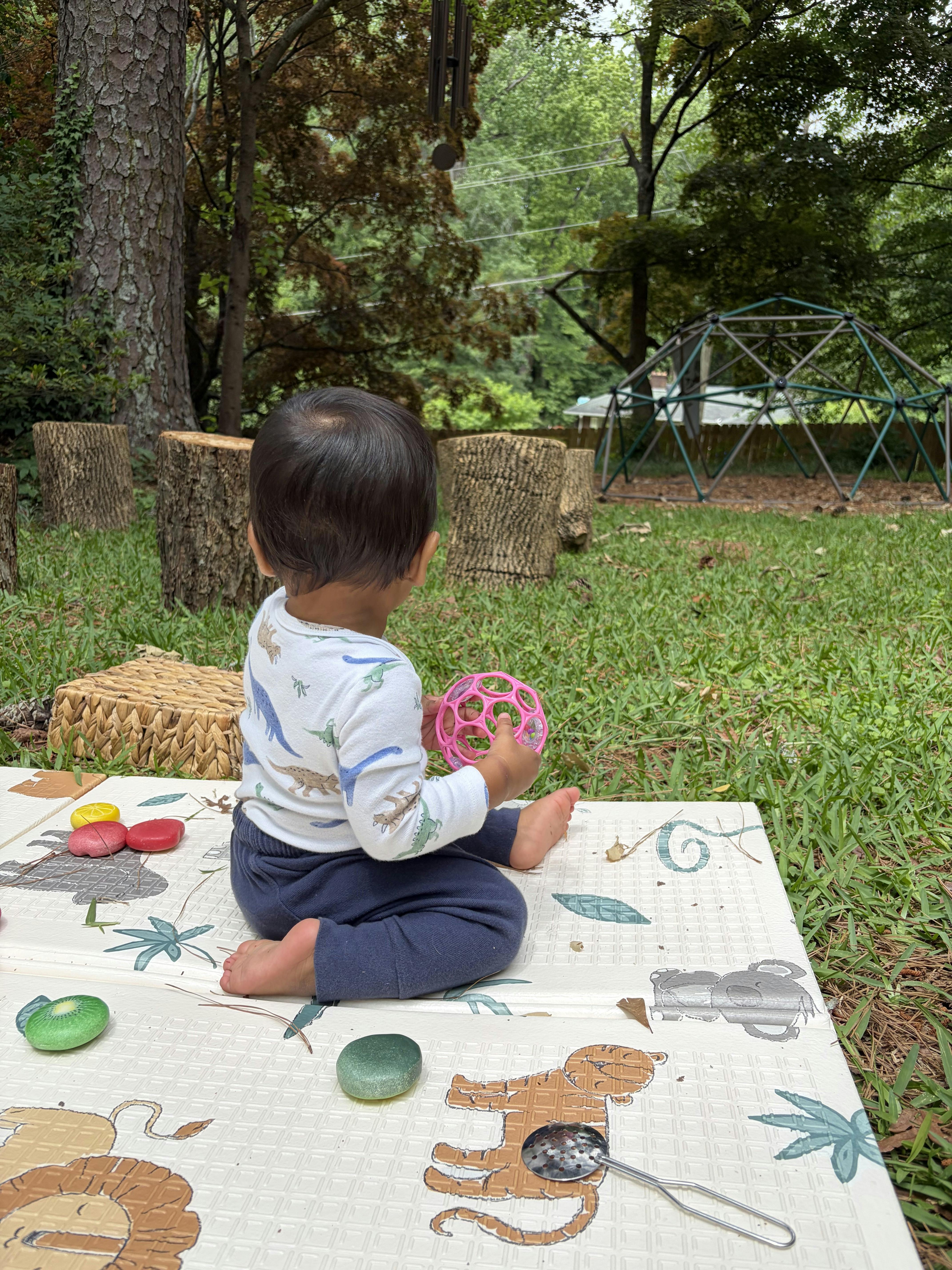 Child sitting on an outdoor play mat with a toy