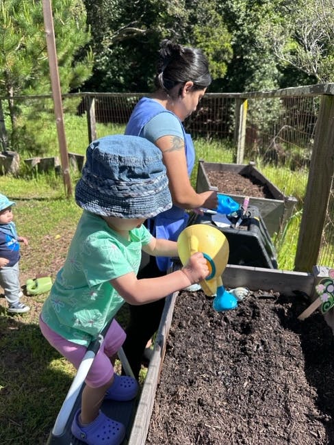 Person and child watering plants in a garden bed