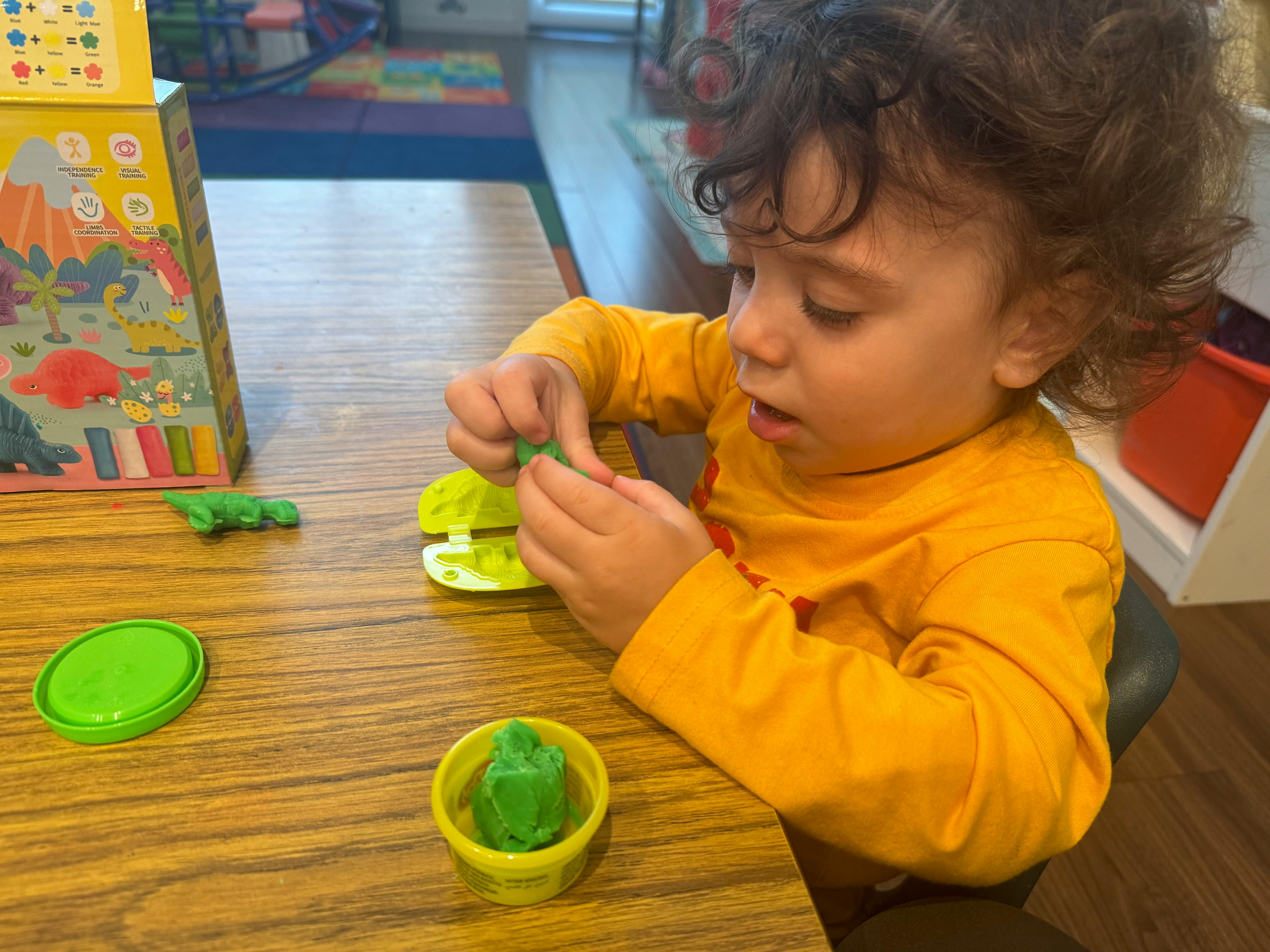 Child playing with green modeling clay at a table