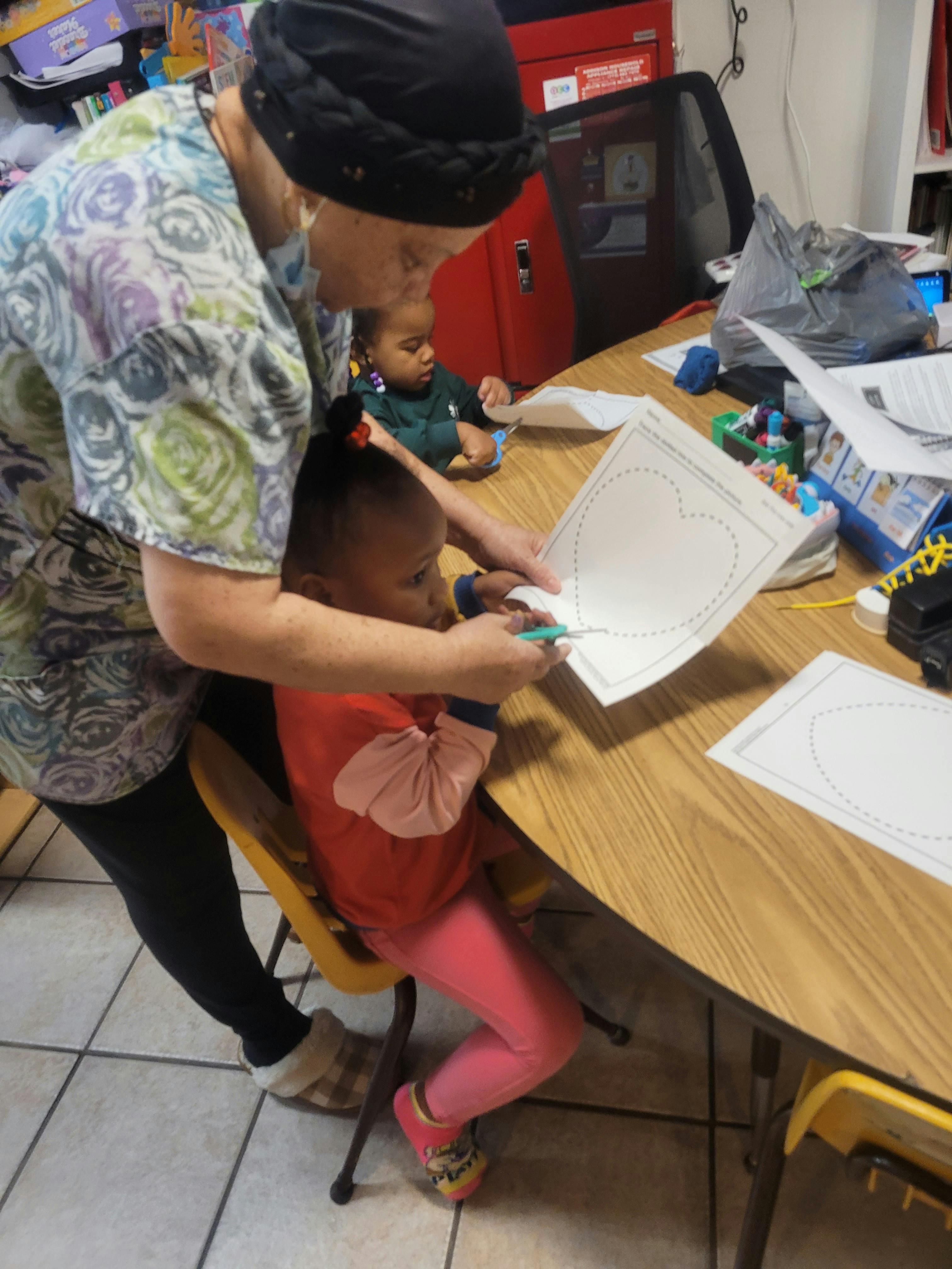 Adult helping a child cut out a paper heart at a table