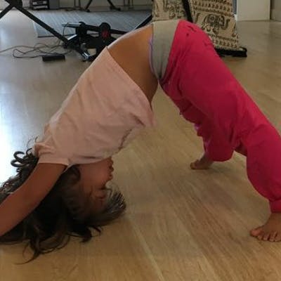 Child in pink shirt and pants doing a yoga pose on a wooden floor