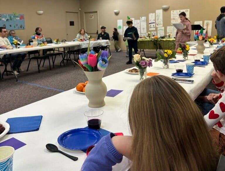 People seated at tables with a person standing and reading in the background
