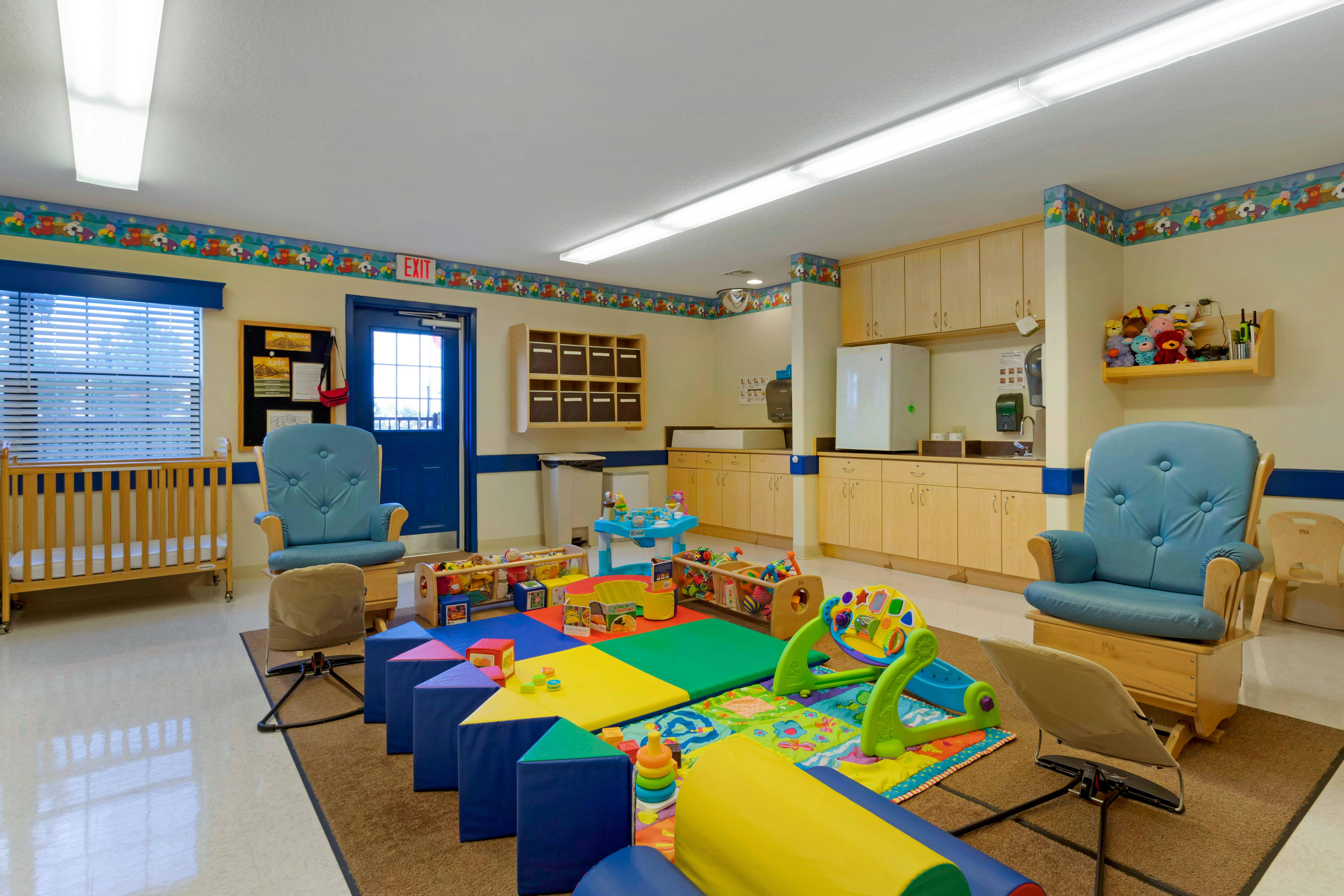 A colorful childcare classroom with a crib, rocking chairs, and play mats