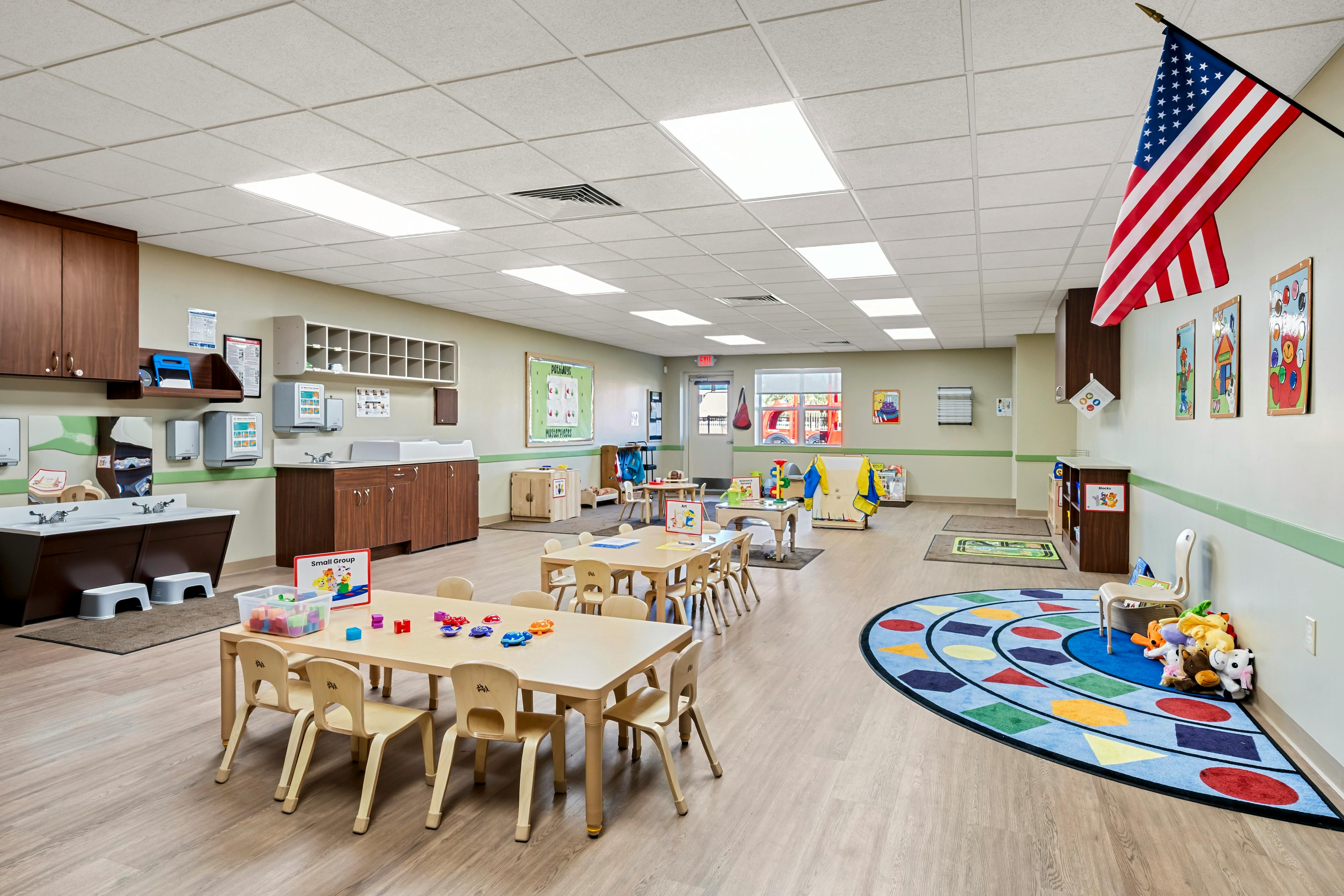 Classroom with child-sized tables and chairs, a sink area, and an American flag