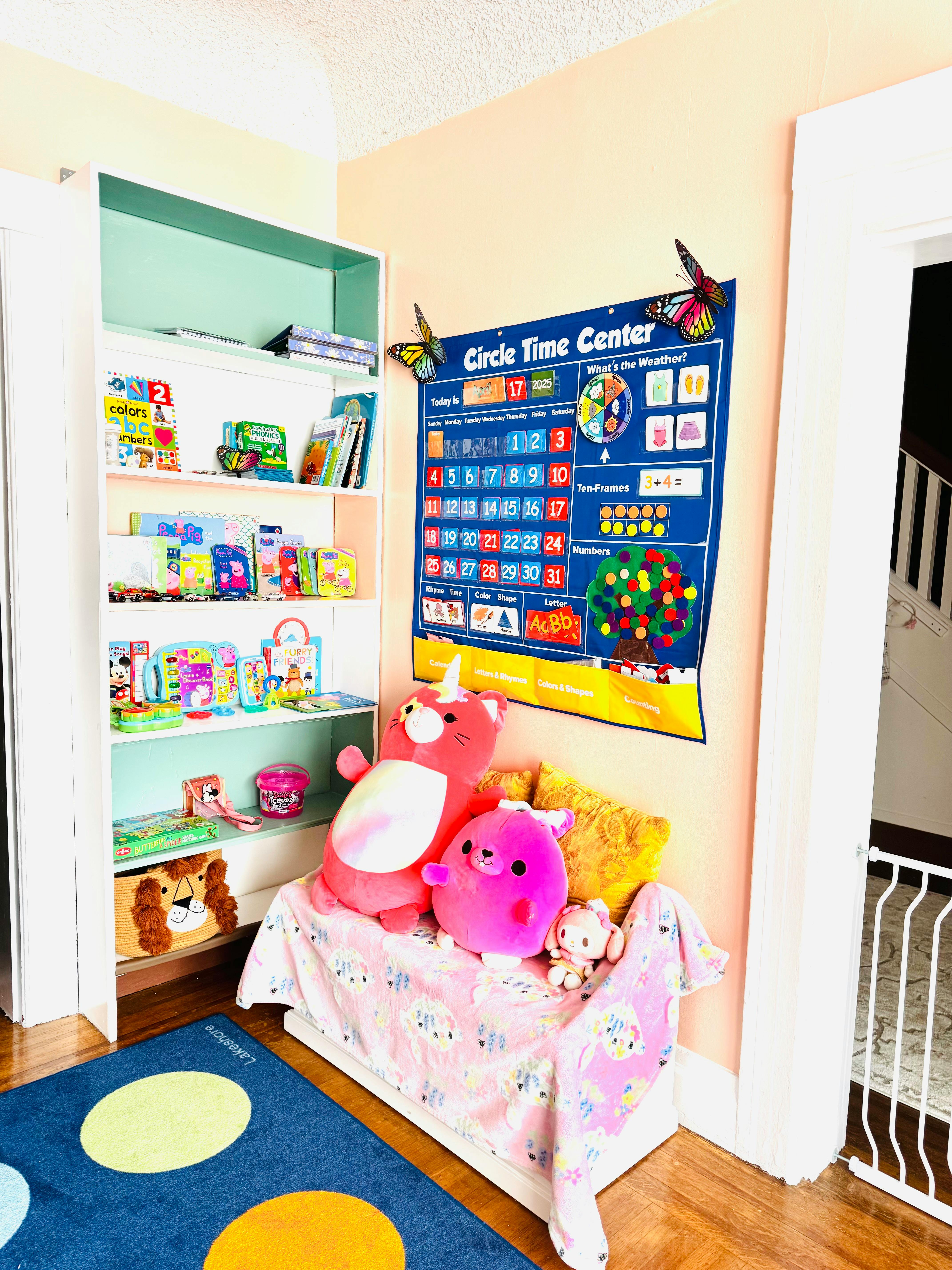 Bookshelf with books and toys next to a calendar chart and stuffed animals