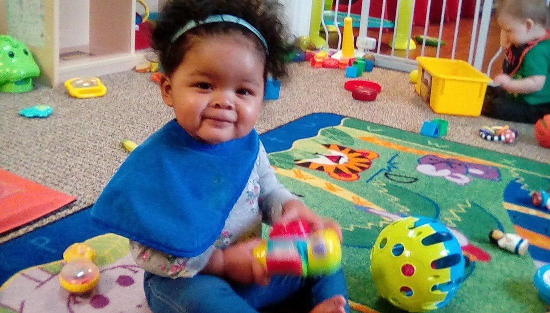Child in a bib playing with toys on a rug