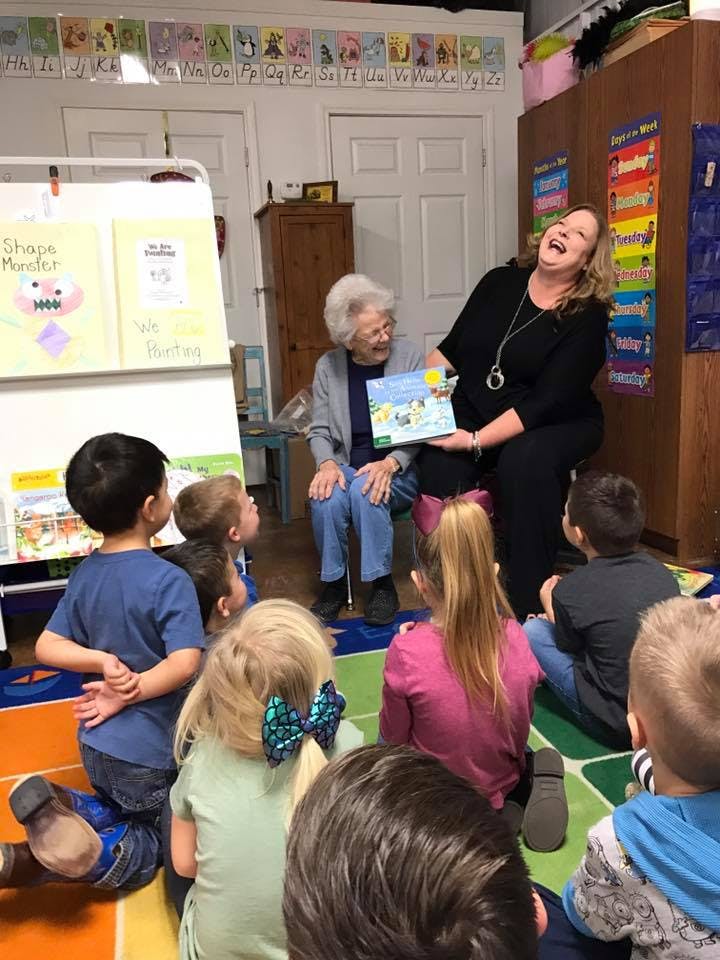 Two adults reading a book to a group of children in a classroom