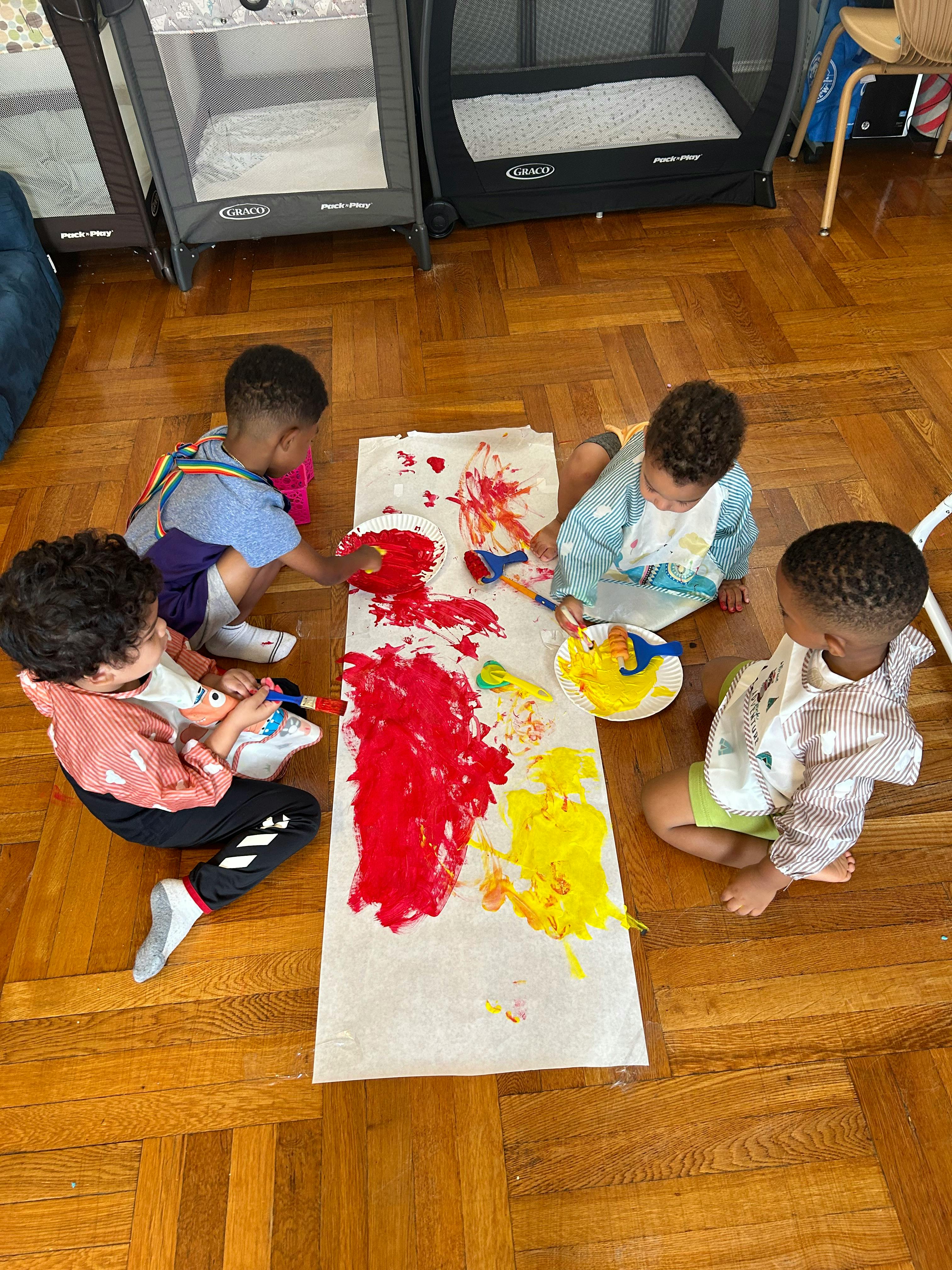 Four children painting on a long sheet of paper on the floor