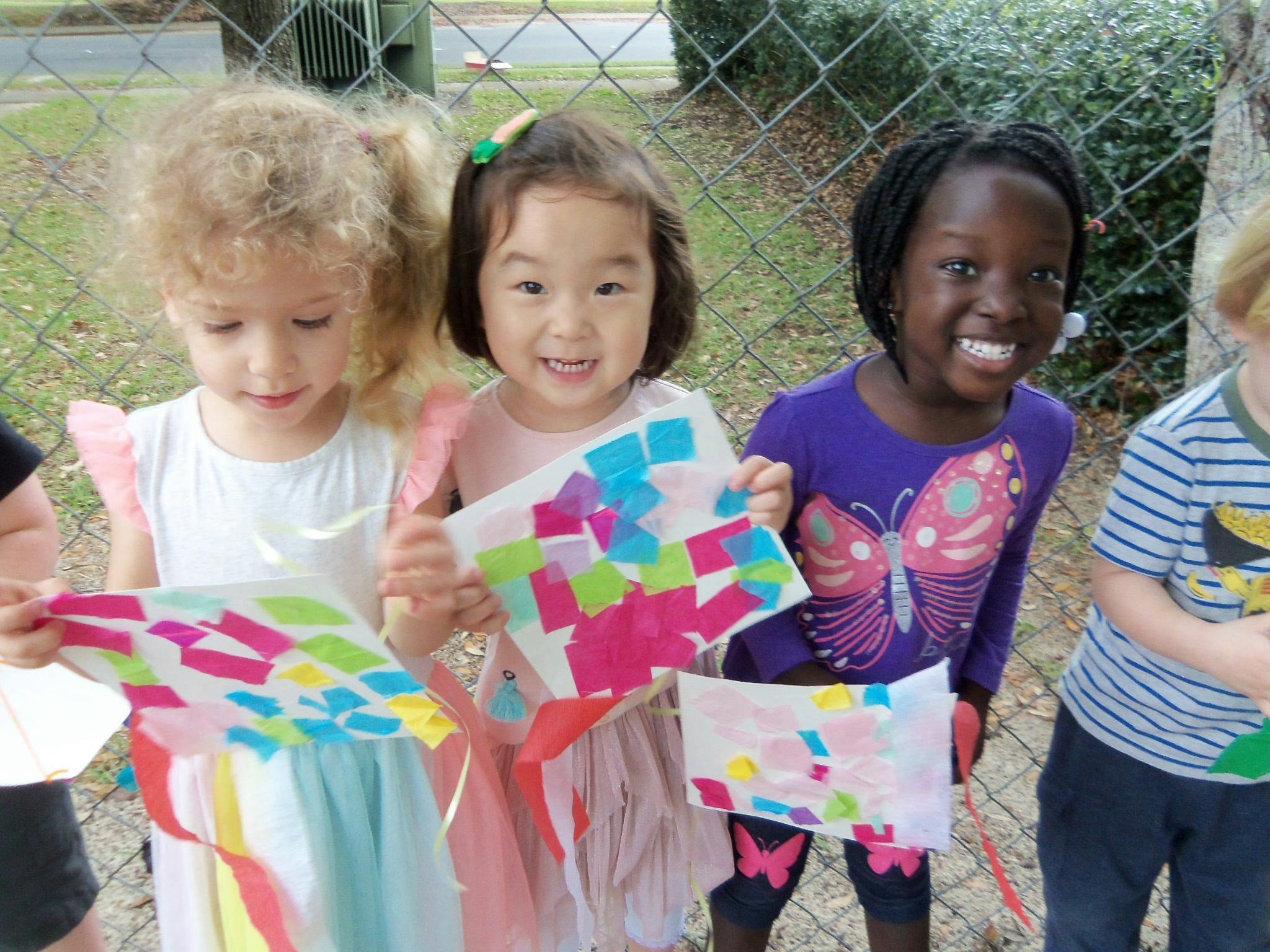 Three children holding up colorful paper crafts