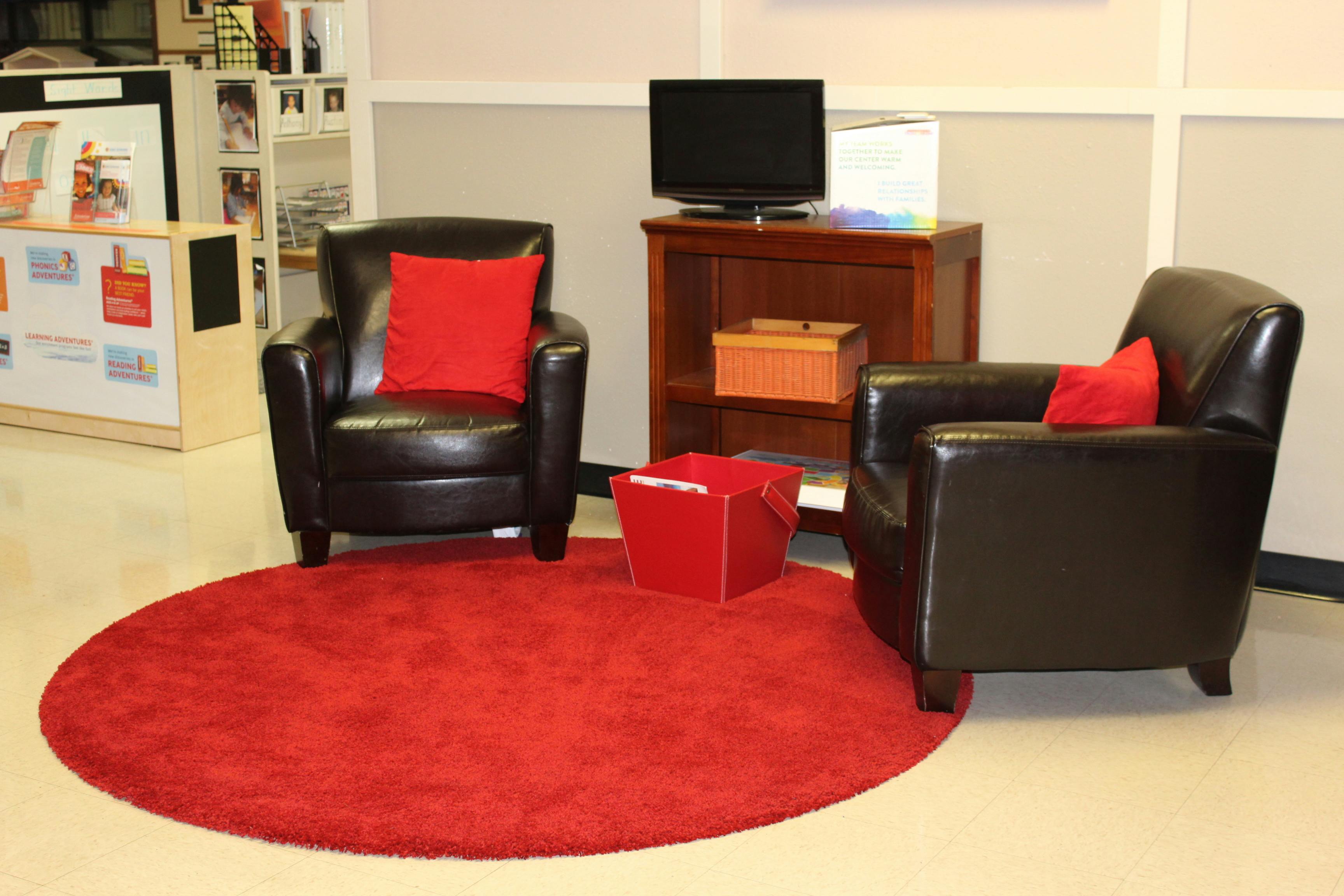 Two brown chairs with red pillows on a red round rug with a TV on a bookshelf