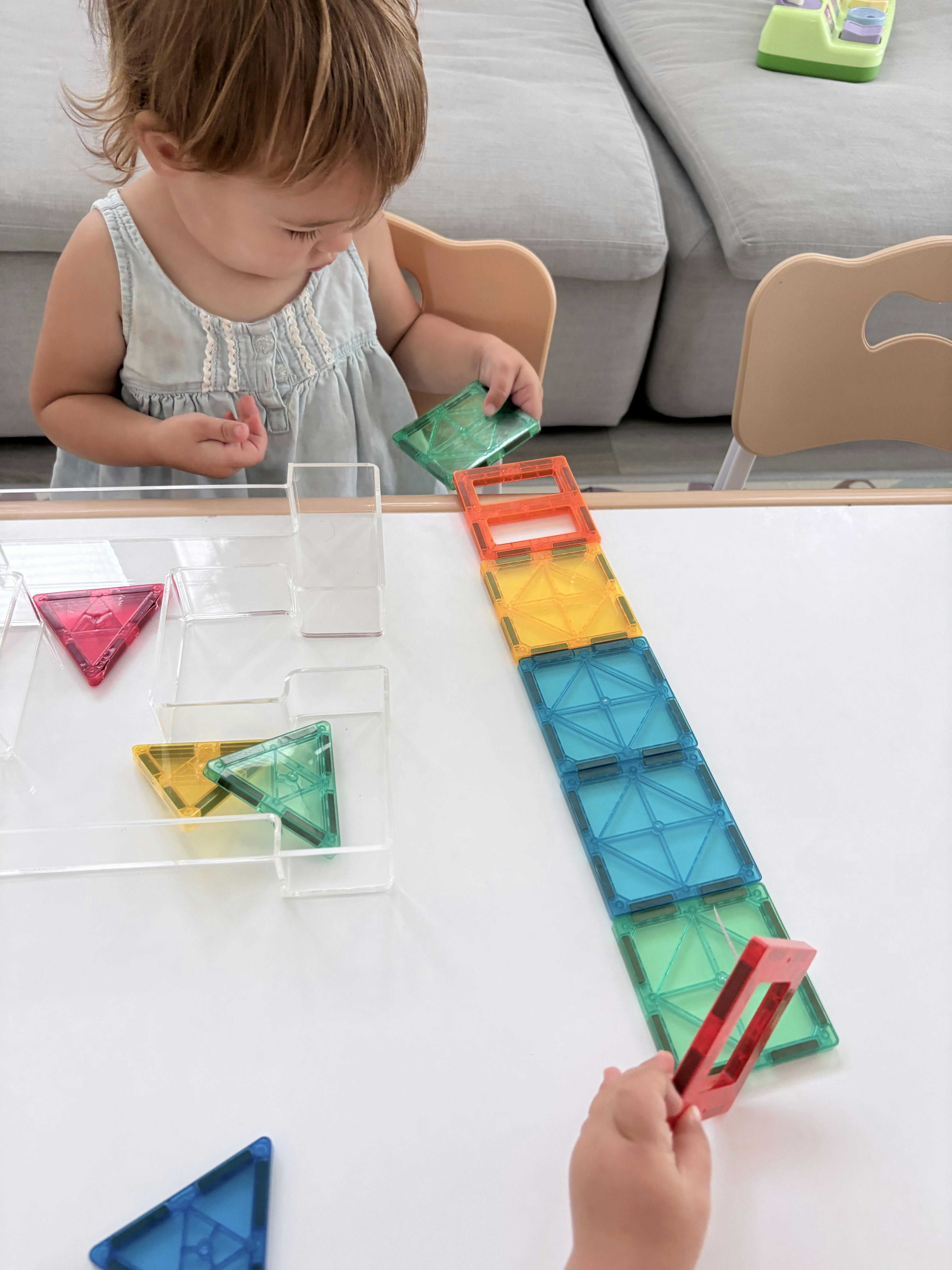 Child playing with colorful magnetic building tiles on a table