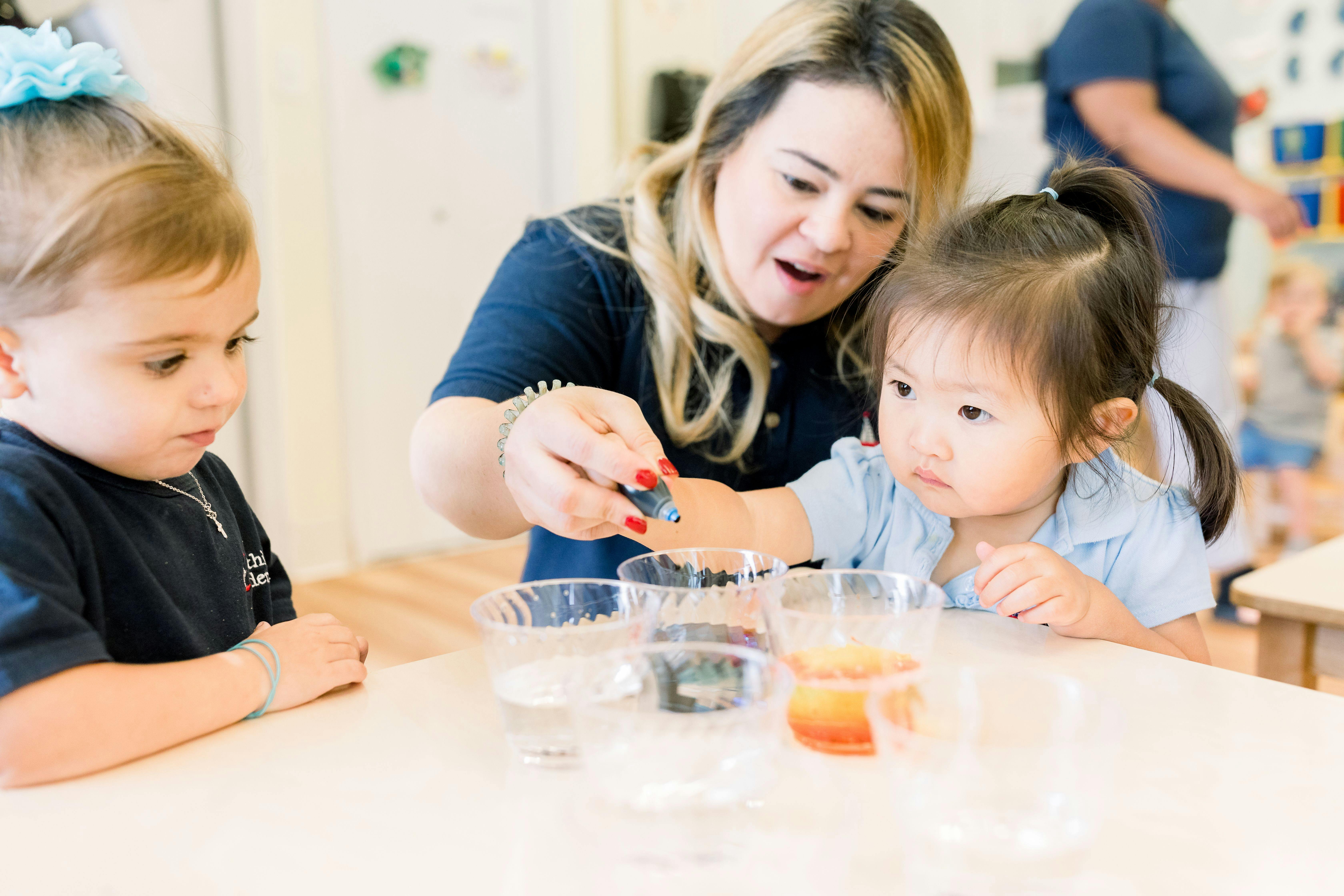 Adult and two children at a table with cups, adding liquid from a dropper