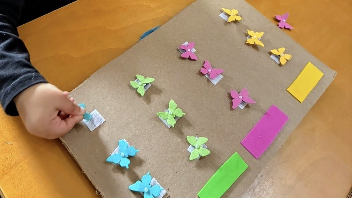 Child's hand placing a blue butterfly cutout on cardboard with other cutouts