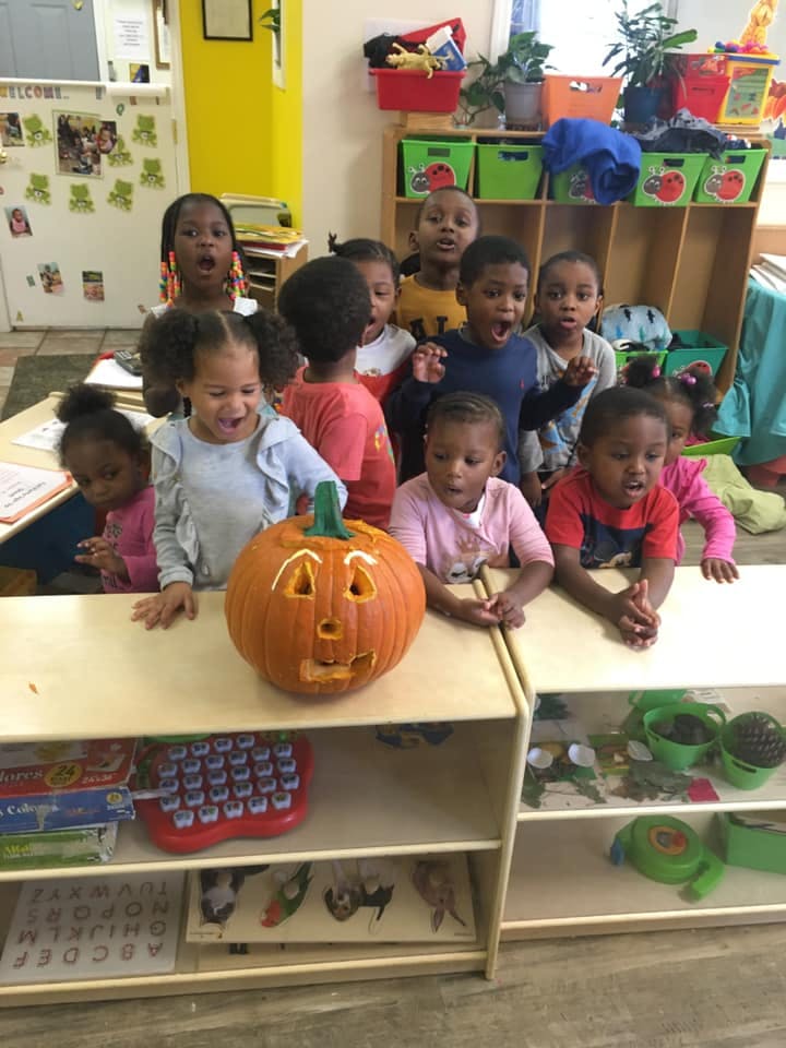 Children gathered around a carved pumpkin in a classroom