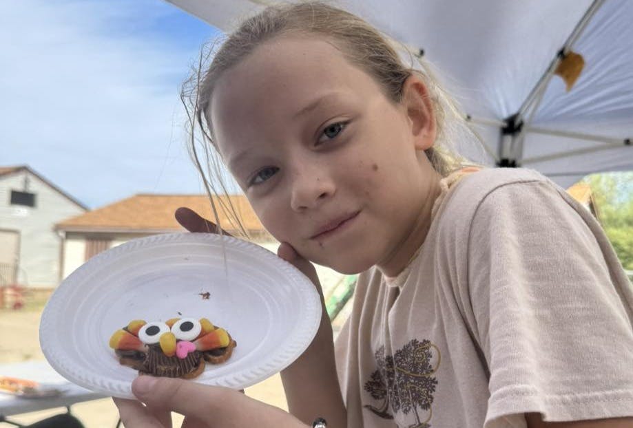 Child holding a paper plate with a cupcake decorated like a turkey