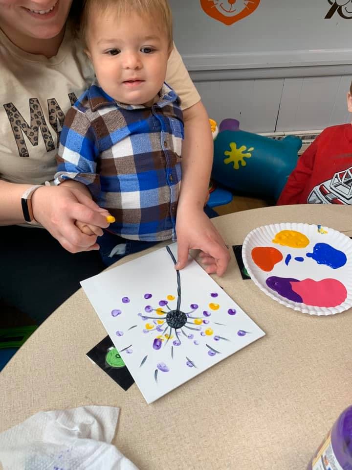 Person holding a child who is finger painting a dandelion
