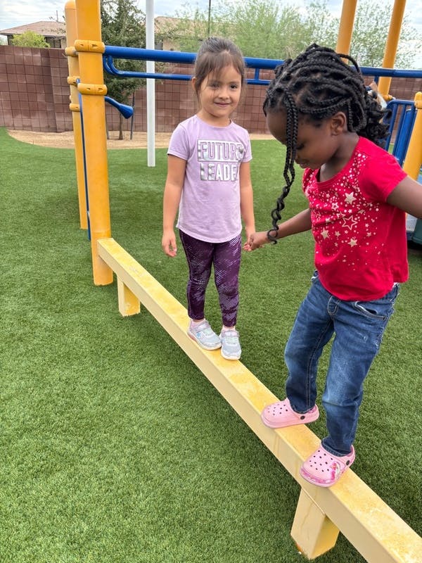 Two children holding hands while walking on a balance beam on a playground