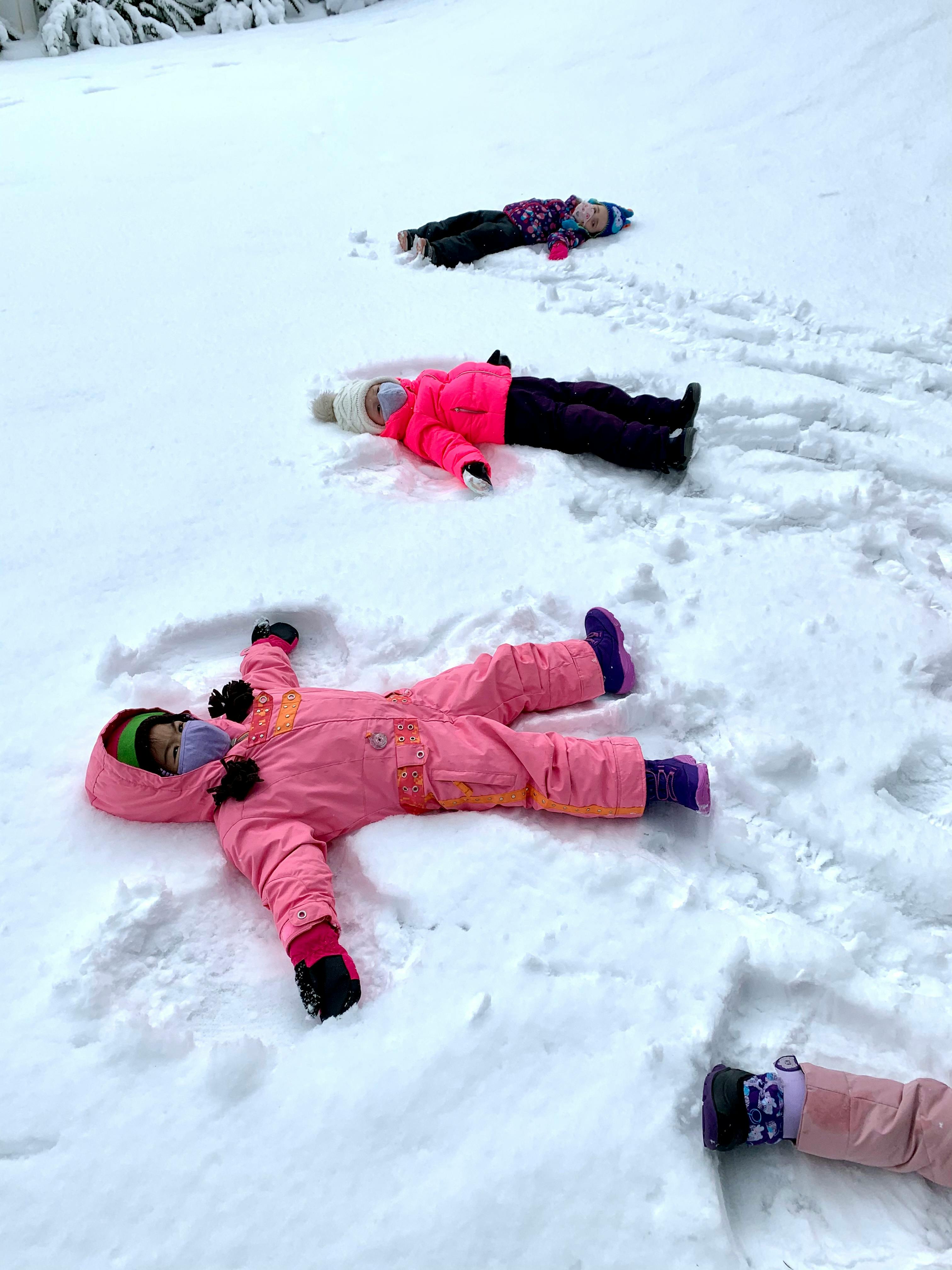 Three children lying in the snow making snow angels