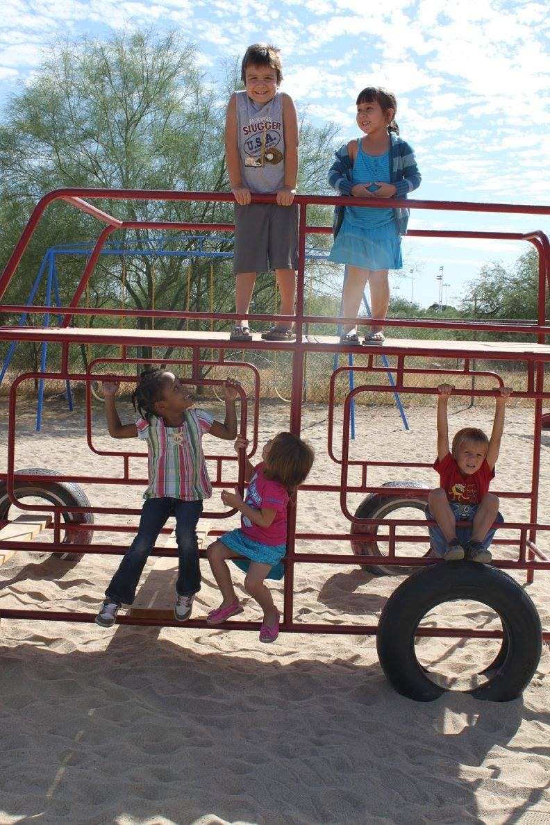 Four children and one teen playing on a red metal playground structure