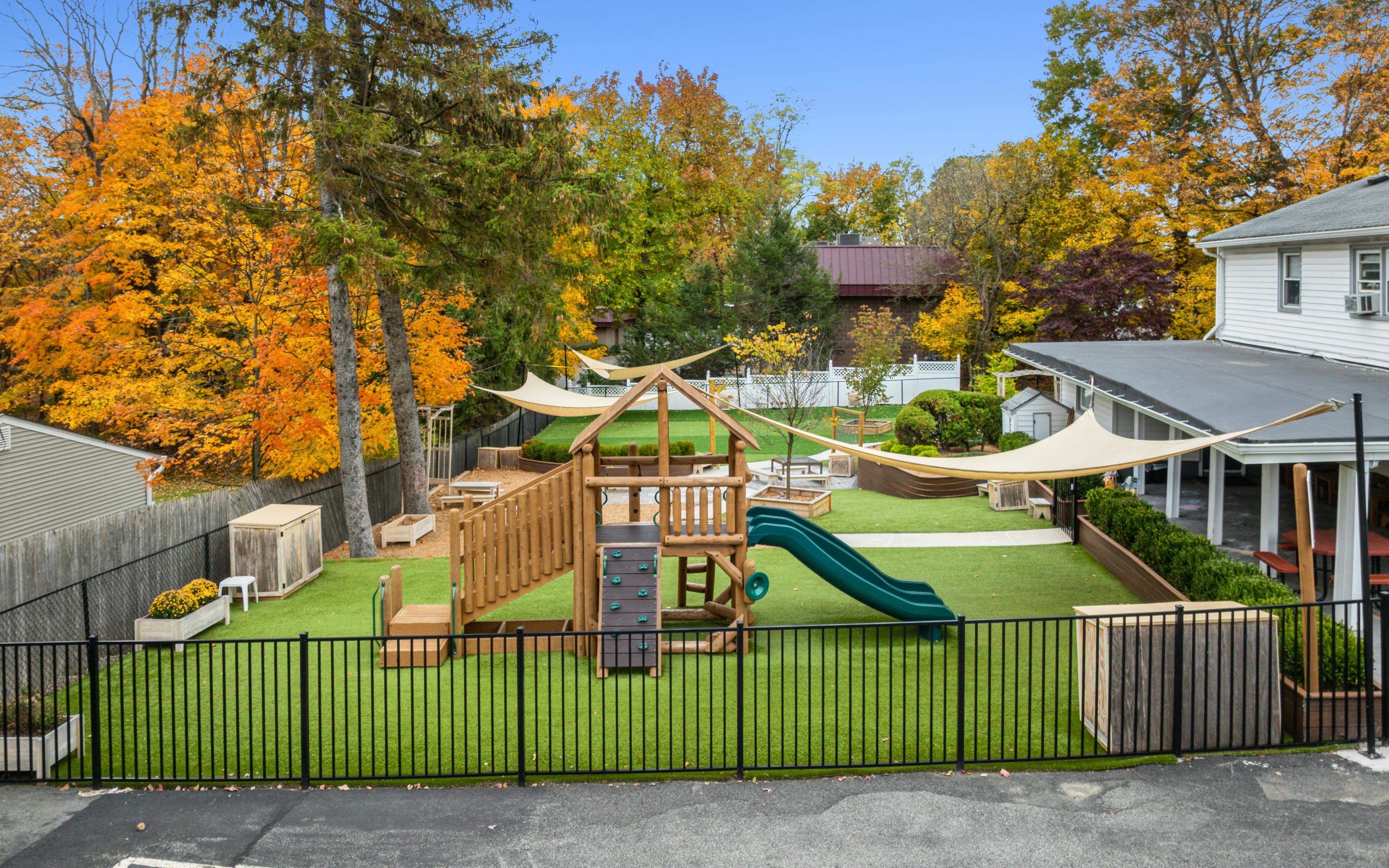 Outdoor playground with artificial turf, wooden play structure, and green slide