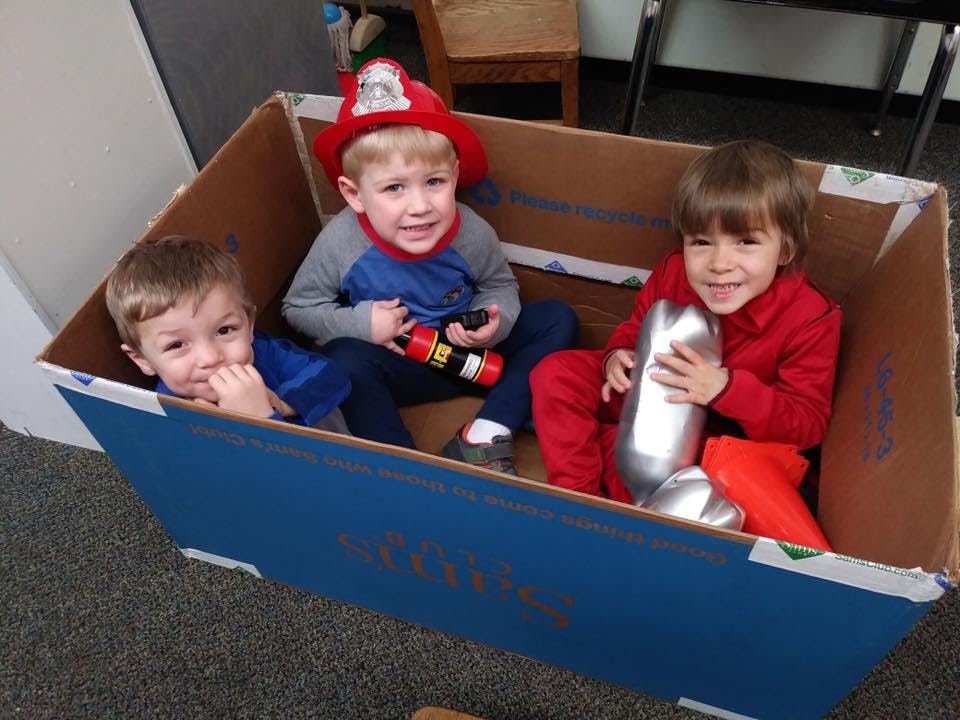 Three children playing in a cardboard box