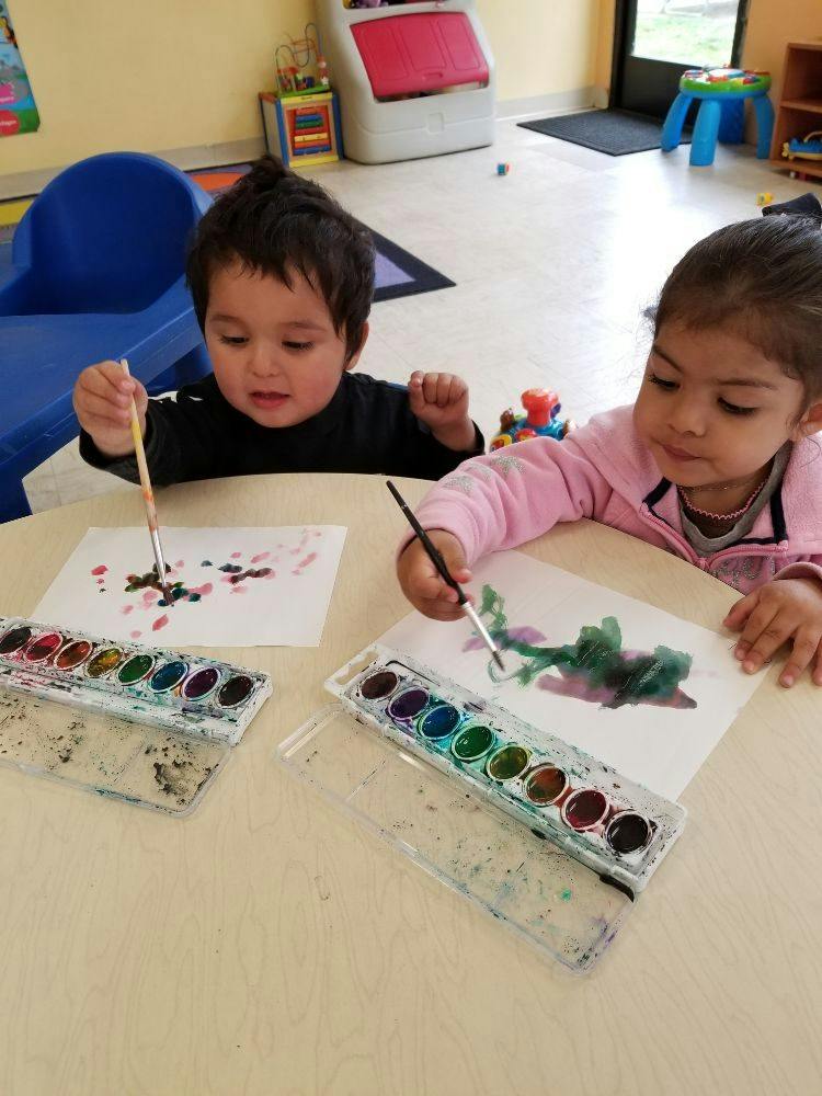 Two children painting with watercolors at a table