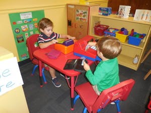 Two children playing with toys at a small table in a classroom