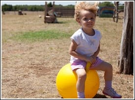 Child sitting on a yellow bouncy ball outdoors