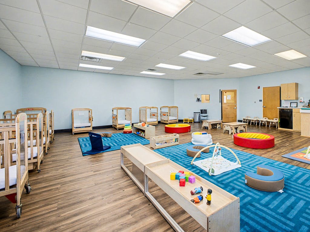 A childcare room with cribs, play mats, and small tables and chairs