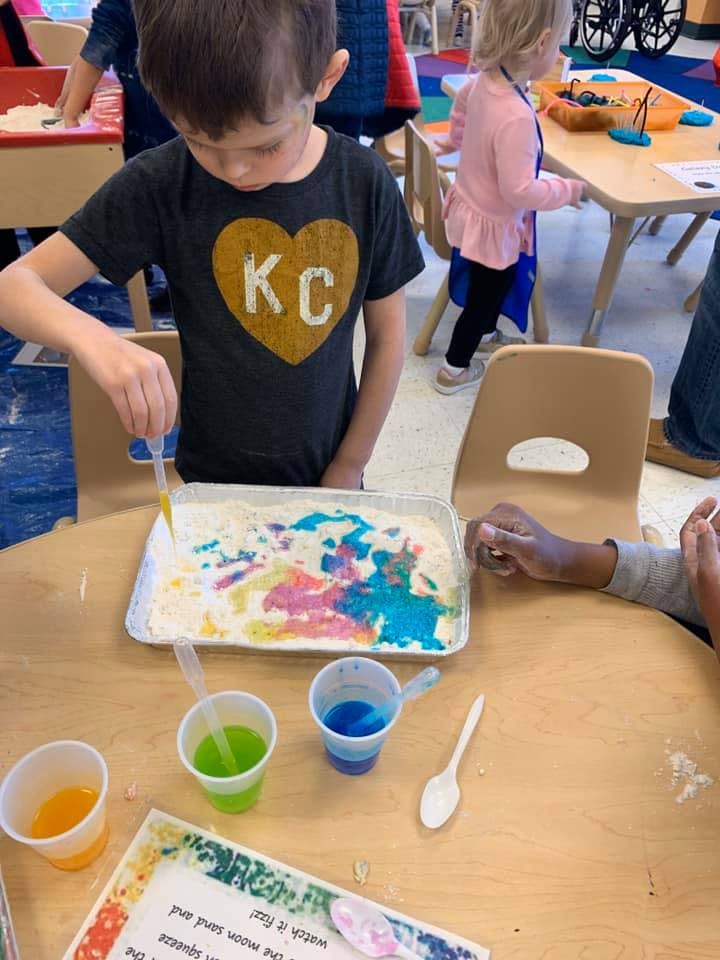 Child using a dropper to add colored liquid to a tray of white material