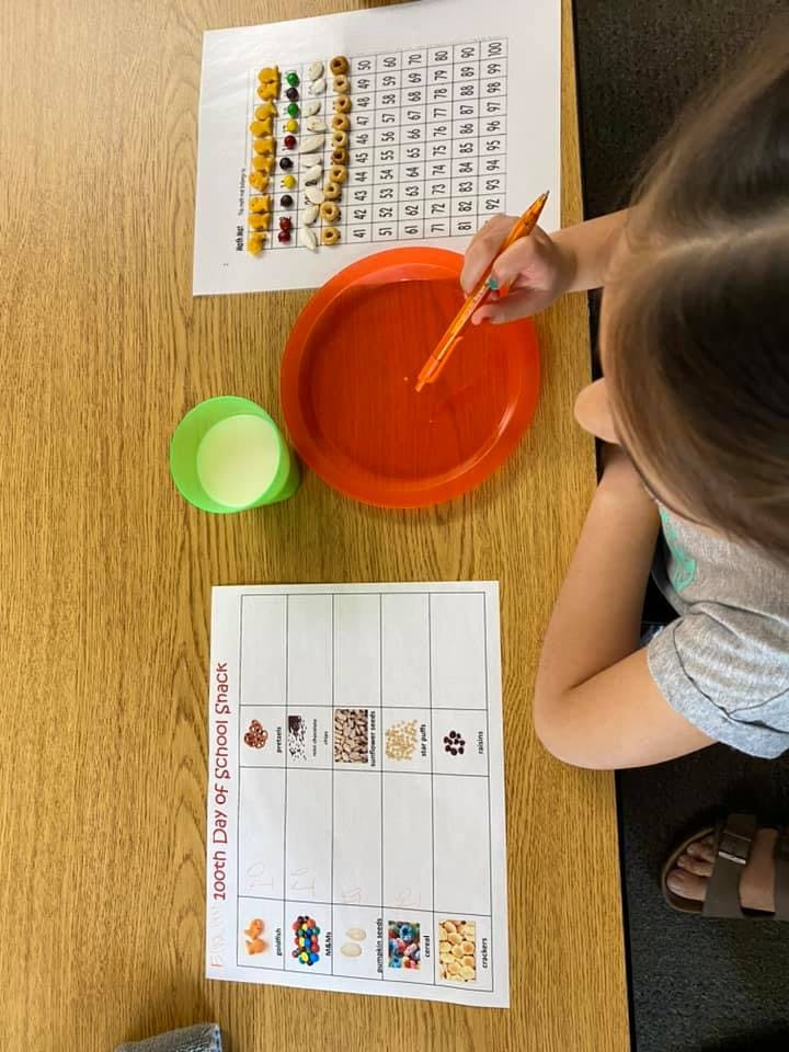 Child using a pen to point at a red plate on a wooden table