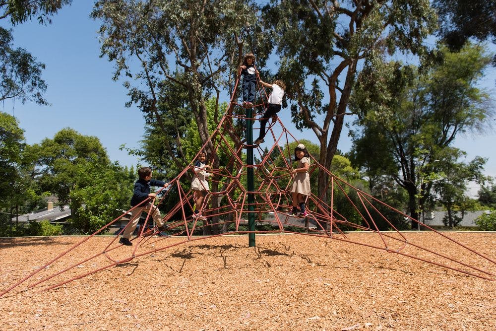 Children climbing on a rope pyramid structure at a playground