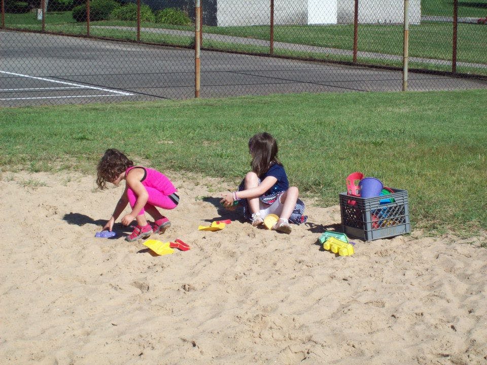 Two children playing in a sandbox with toys