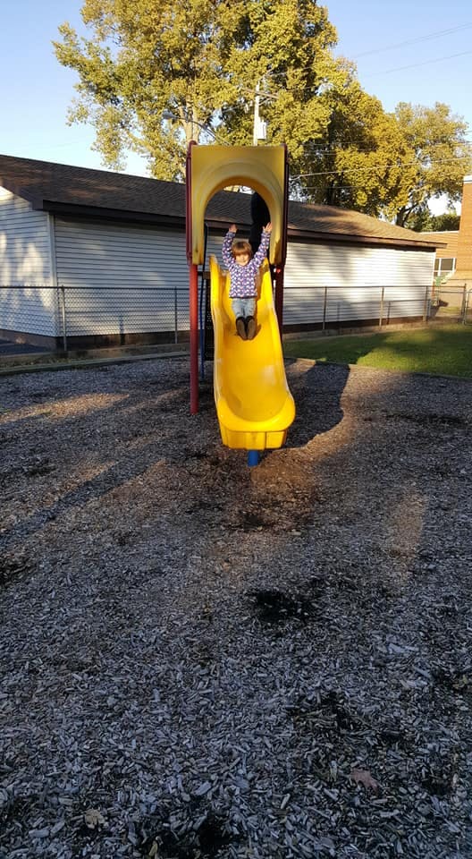 Child on a yellow slide with arms raised in a playground