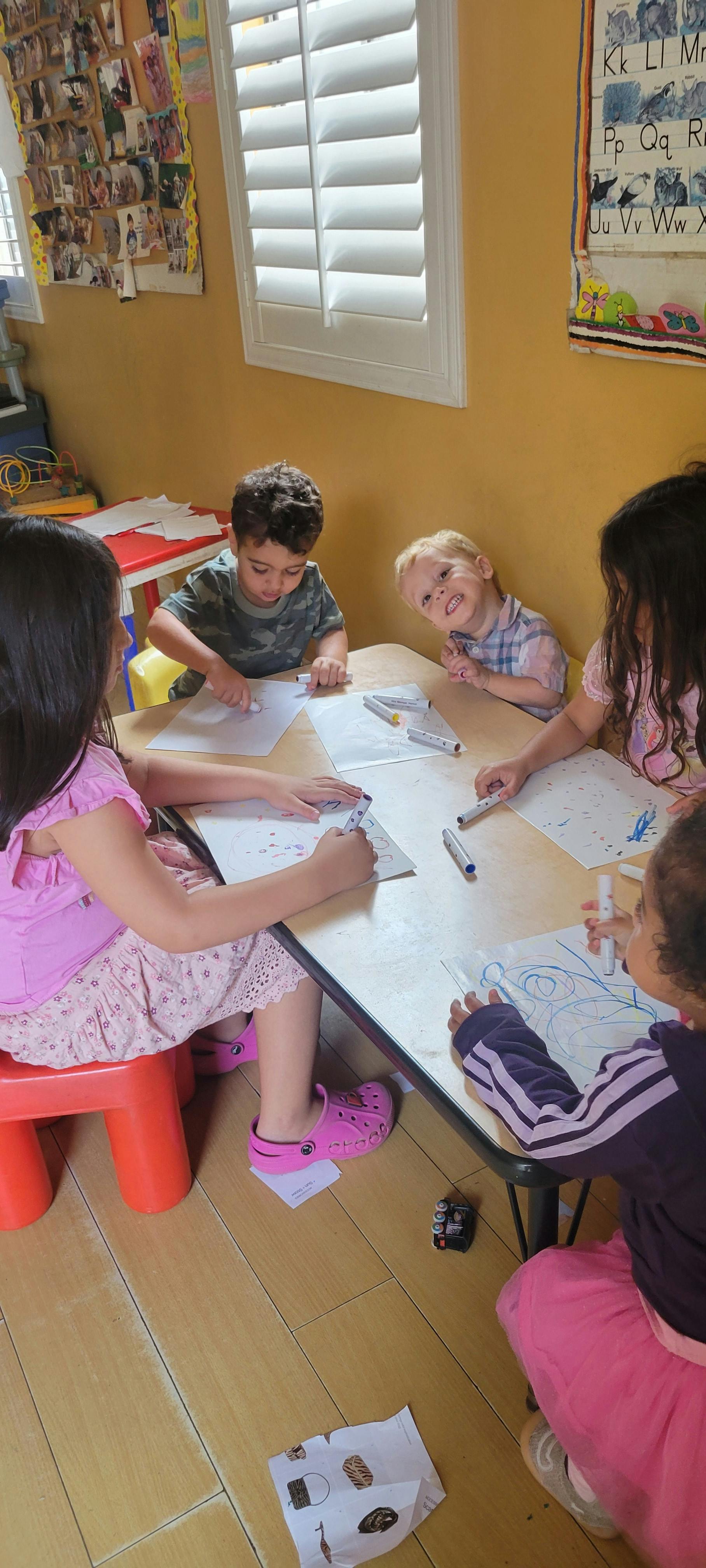 Children sitting at a table drawing on paper with markers in a classroom