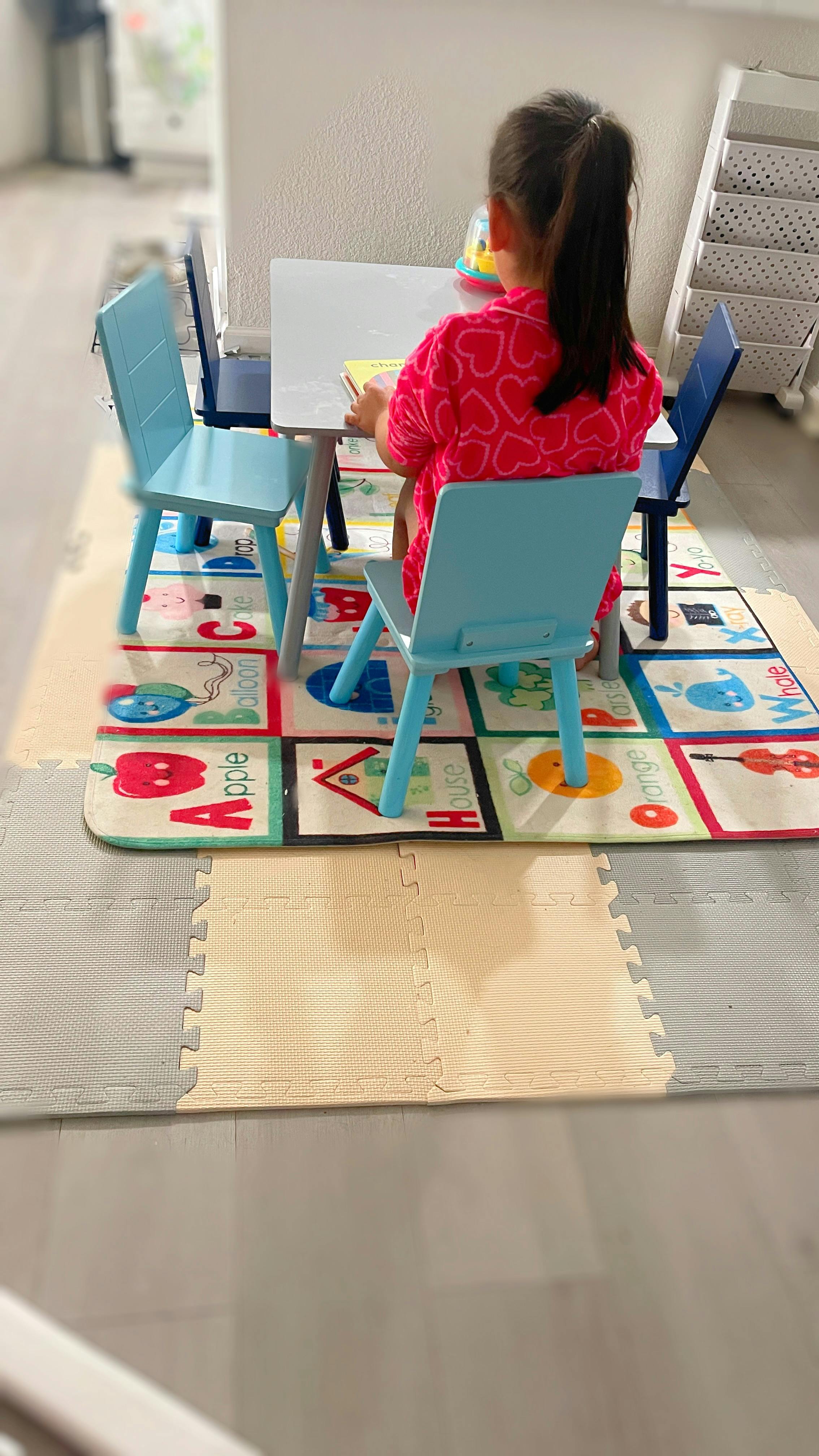 Child sitting at a small table with chairs on an alphabet playmat