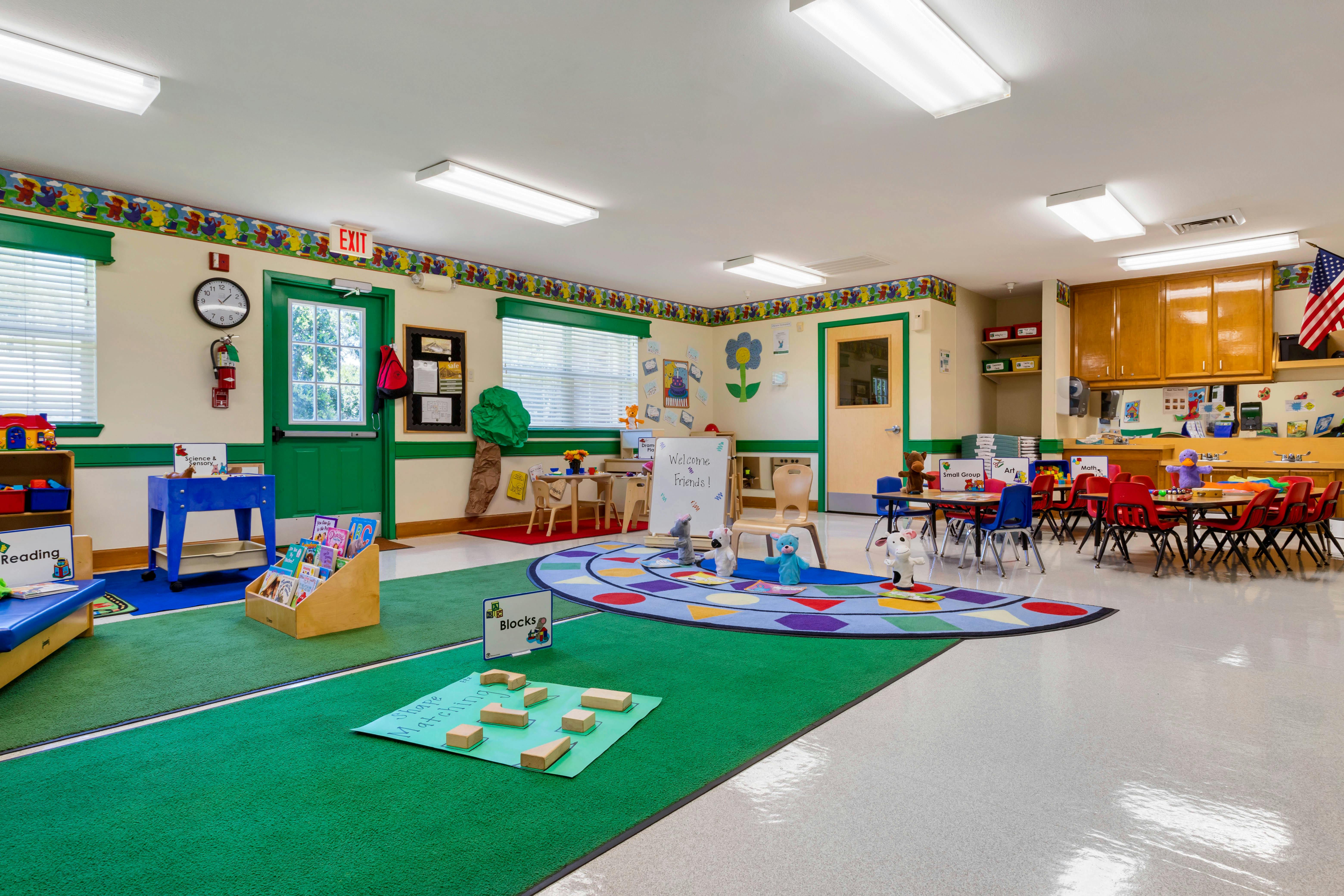 Classroom with small tables and chairs, a book display, and a colorful rug