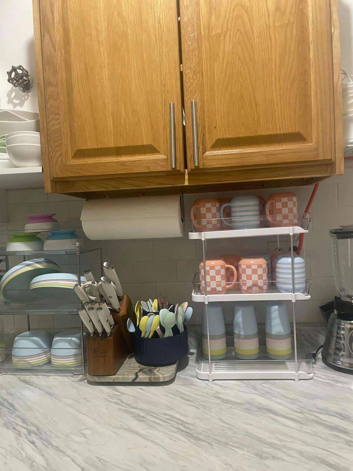 Kitchen counter with dishes, utensils, and mugs under wooden cabinets
