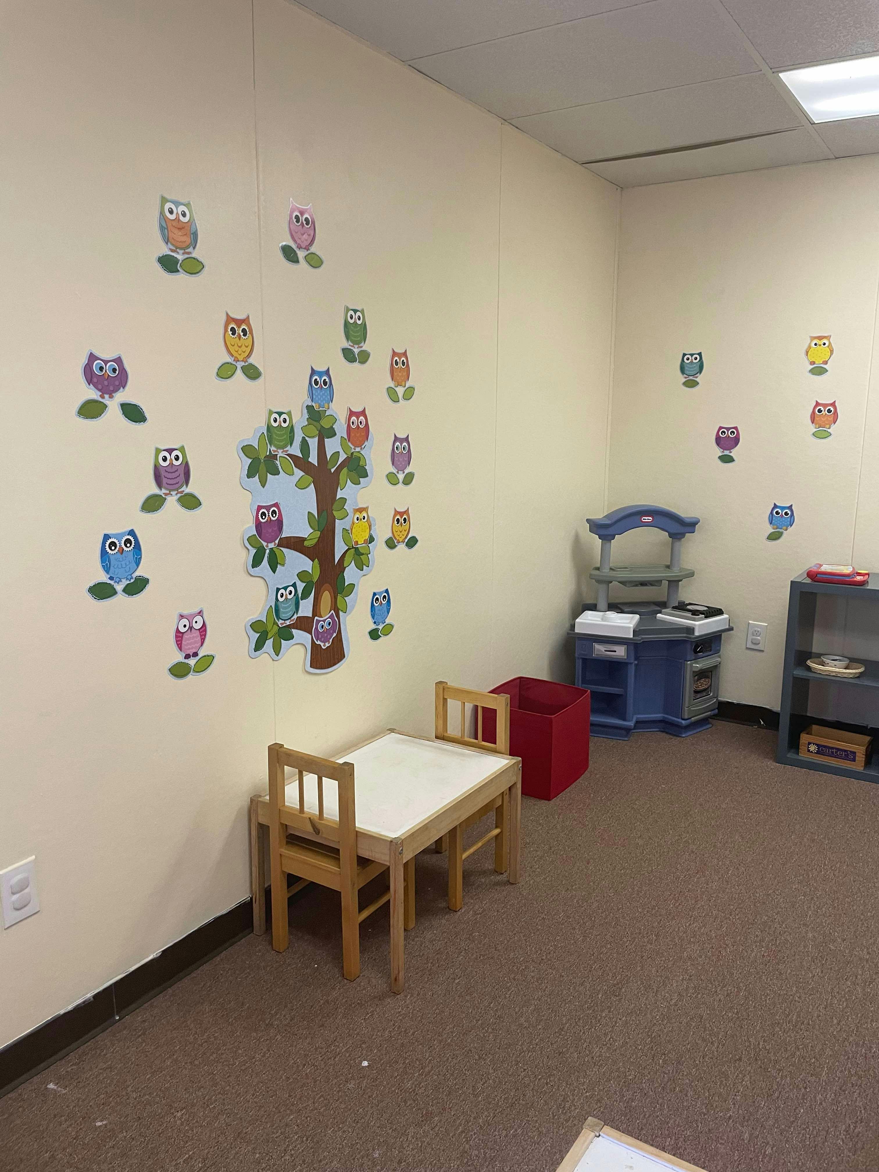 Classroom with owl wall decals, small table and chairs, and play kitchen