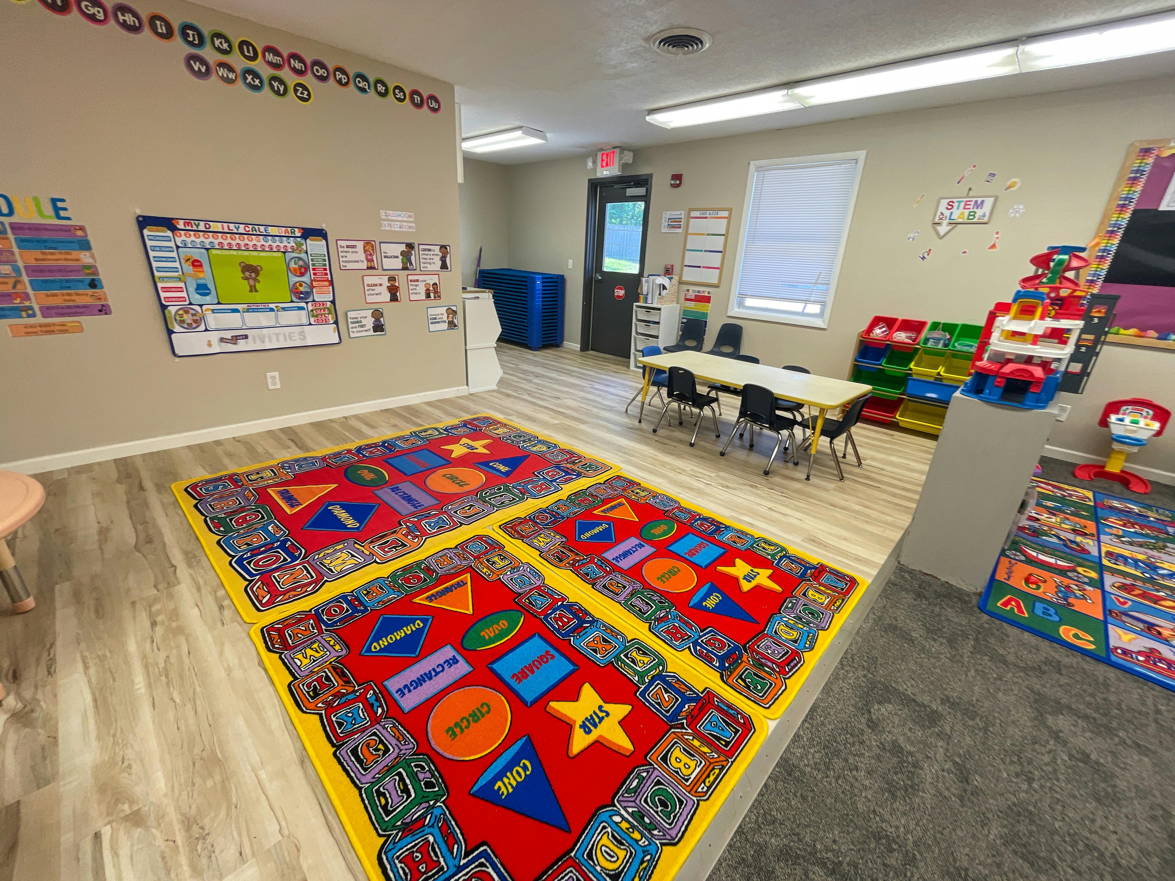 Classroom with colorful rugs, tables, and learning materials on walls