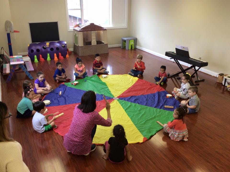 Adult and children sitting on a colorful parachute on a wooden floor