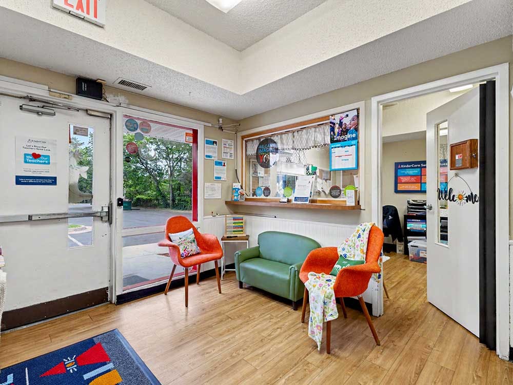 waiting area with two orange chairs, a green couch, and a reception window