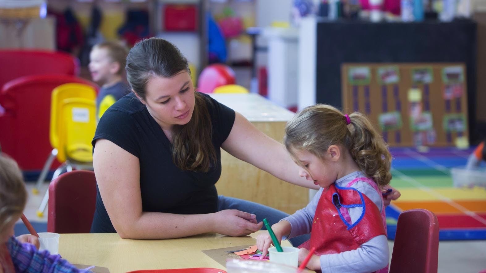 Adult and child drawing at a table in a classroom