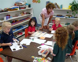 Adult supervising children doing crafts at a table in a classroom