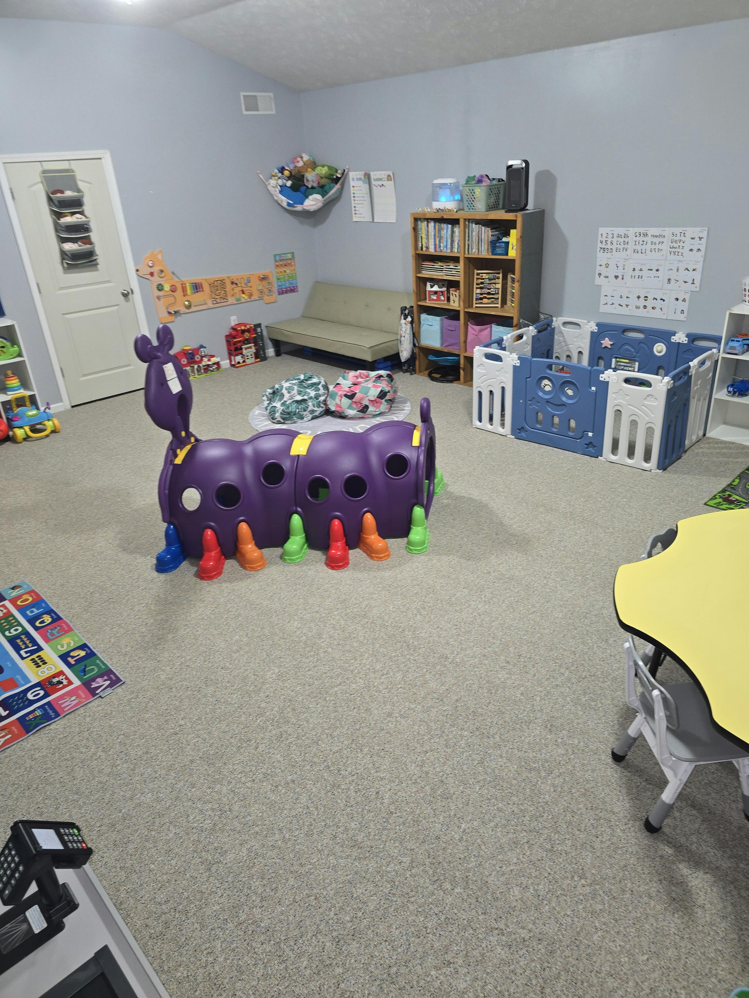 Playroom with a purple caterpillar tunnel, toy storage, and children furniture